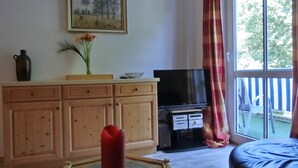Ein Wohnzimmer mit Fernseher, Holzschränken, einer Blumenvase und einem großen Fenster mit Vorhängen.