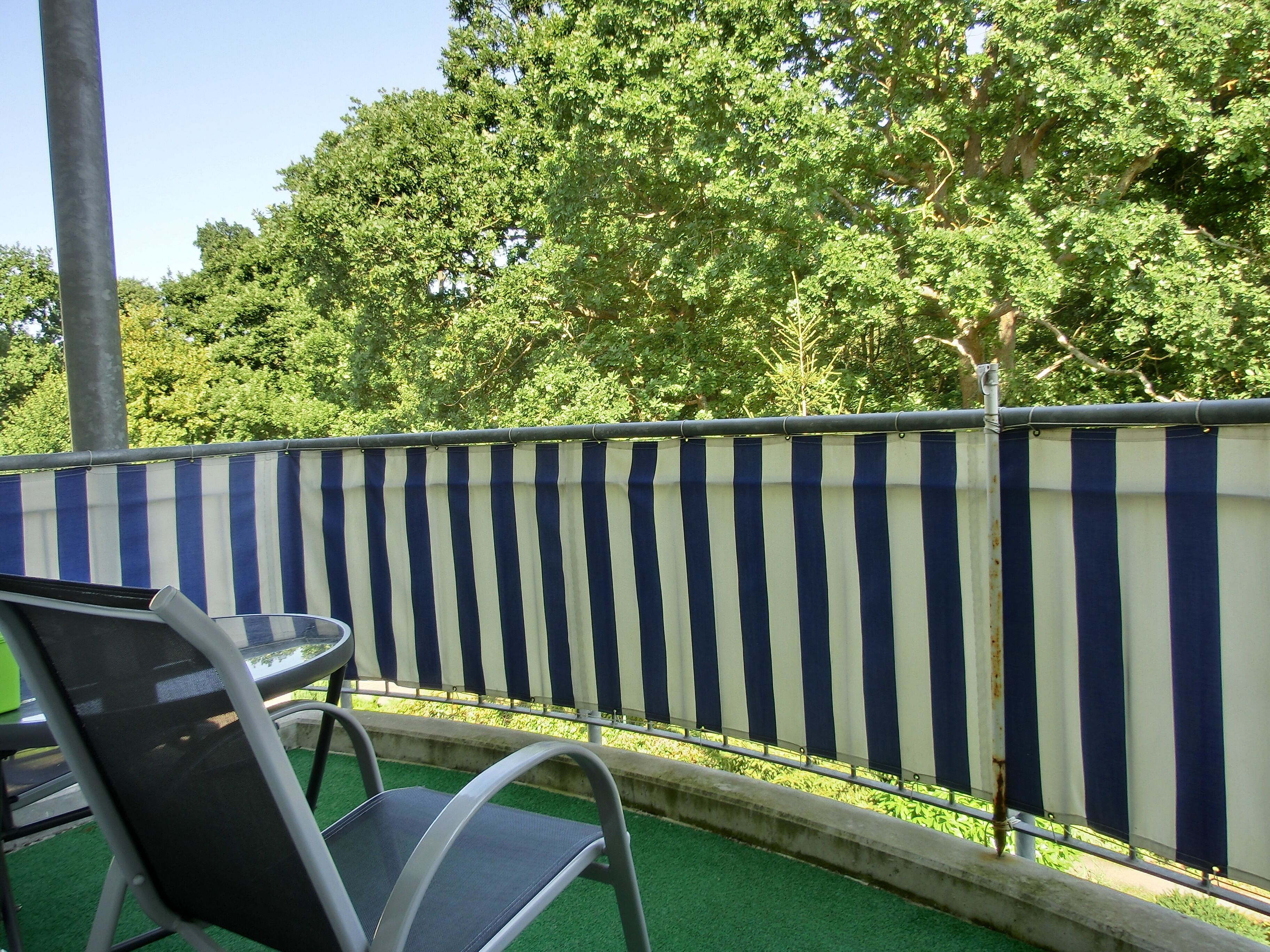 A balcony with a striped metal fence, a metal chair, and a small round table.