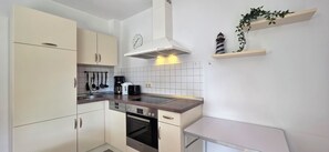 A modern kitchen with a Bosch oven, a coffee maker, and a toaster. There are cabinets, a sink, and a clock on the wall.
