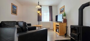 A furnished living room with a sofa, a television, a wooden cabinet, a fireplace, and a radiator. - 3-room apartment on the 1st floor, suitable for 6 people.   (Graal-Müritz)