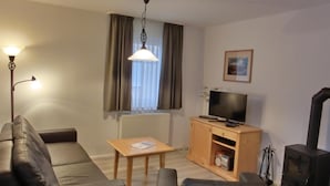 A living room with a sofa, a coffee table, a TV on a wooden cabinet, a fireplace, and a window with curtains. - 3-room apartment on the first floor, suitable for 6 people. (Graal-Müritz)