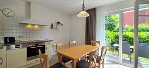 Une cuisine moderne équipée d’un four Bosch, d’une table à manger avec des chaises et offrant une vue sur la verdure grâce à une porte-fenêtre coulissante.