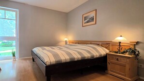A bedroom with a bed, bedside tables, a chair, a window, and a picture on the wall. - 3-room apartment on the first floor, suitable for 6 people. (Graal-Müritz)