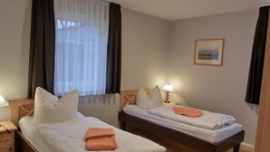 A hotel room with two single beds, a nightstand with a lamp, a window with curtains, and a framed picture on the wall. - 3-room apartment on the first floor, suitable for 6 people. (Graal-Müritz)