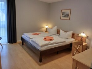 Uma cama de casal com toalhas brancas e cor-de-pêssego, duas luminárias de cabeceira e um quadro na parede.