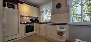 Una cocina moderna con armarios blancos, encimera negra, horno empotrado, microondas, cafetera y ventana con vista a árboles.