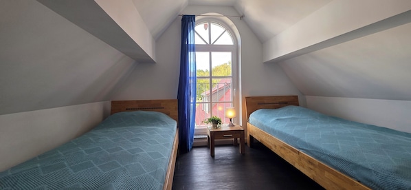 Un dormitorio con dos camas de madera, una mesita de noche con lámpara y una ventana con cortina.