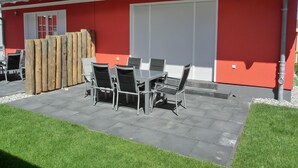 Un patio con una mesa y sillas, un cerco de madera y un edificio rojo con techo gris.