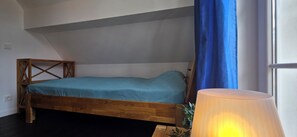 A single bed with a wooden frame and a blue mattress in a room with a sloped ceiling and a window with blue curtains. - Doppelhaushälfte mit ca. 95 m² Wohnfläche für 8 Personen (Graal-Müritz)