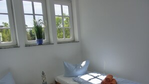 Un dormitorio con cama, mesita de noche, planta en maceta y tres ventanas.