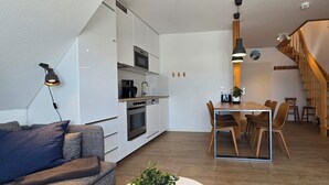 Una cocina moderna con armarios blancos, un comedor con una mesa y sillas de madera, y una escalera que sube a otro nivel.