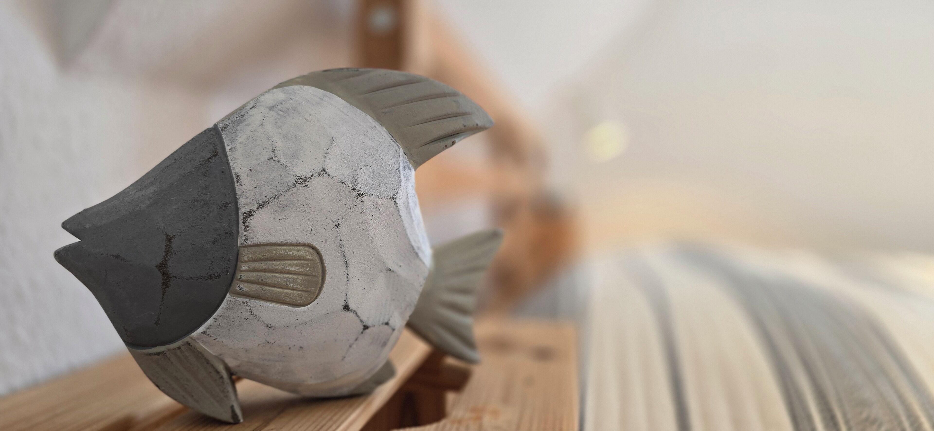 A fish-shaped object with a textured surface, possibly made of stone or concrete, placed on a wooden surface.