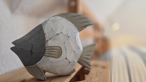 Un objeto con forma de pez, de superficie texturizada, posiblemente de piedra o concreto, sobre una superficie de madera.