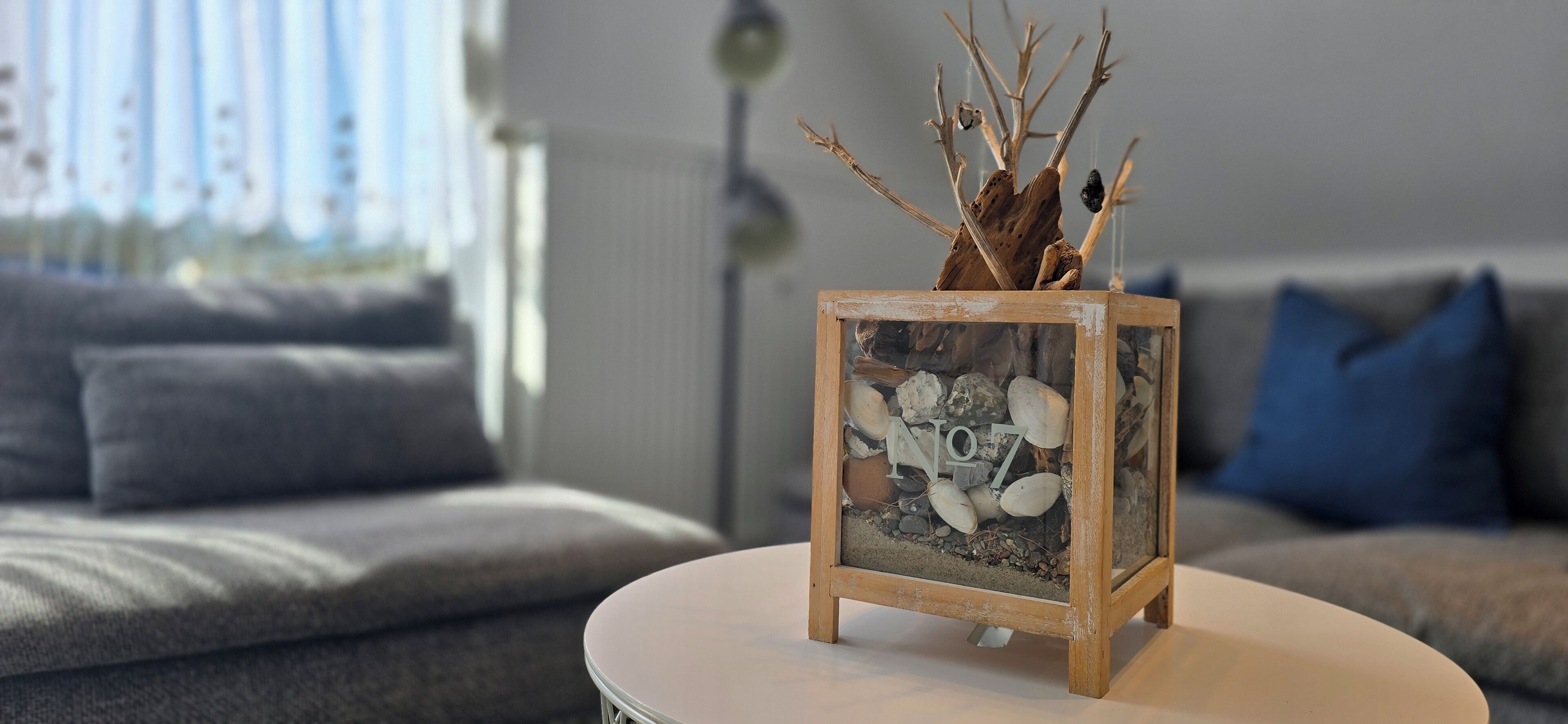 Une petite table en bois sur laquelle repose un terrarium en verre contenant des roches et des branches.