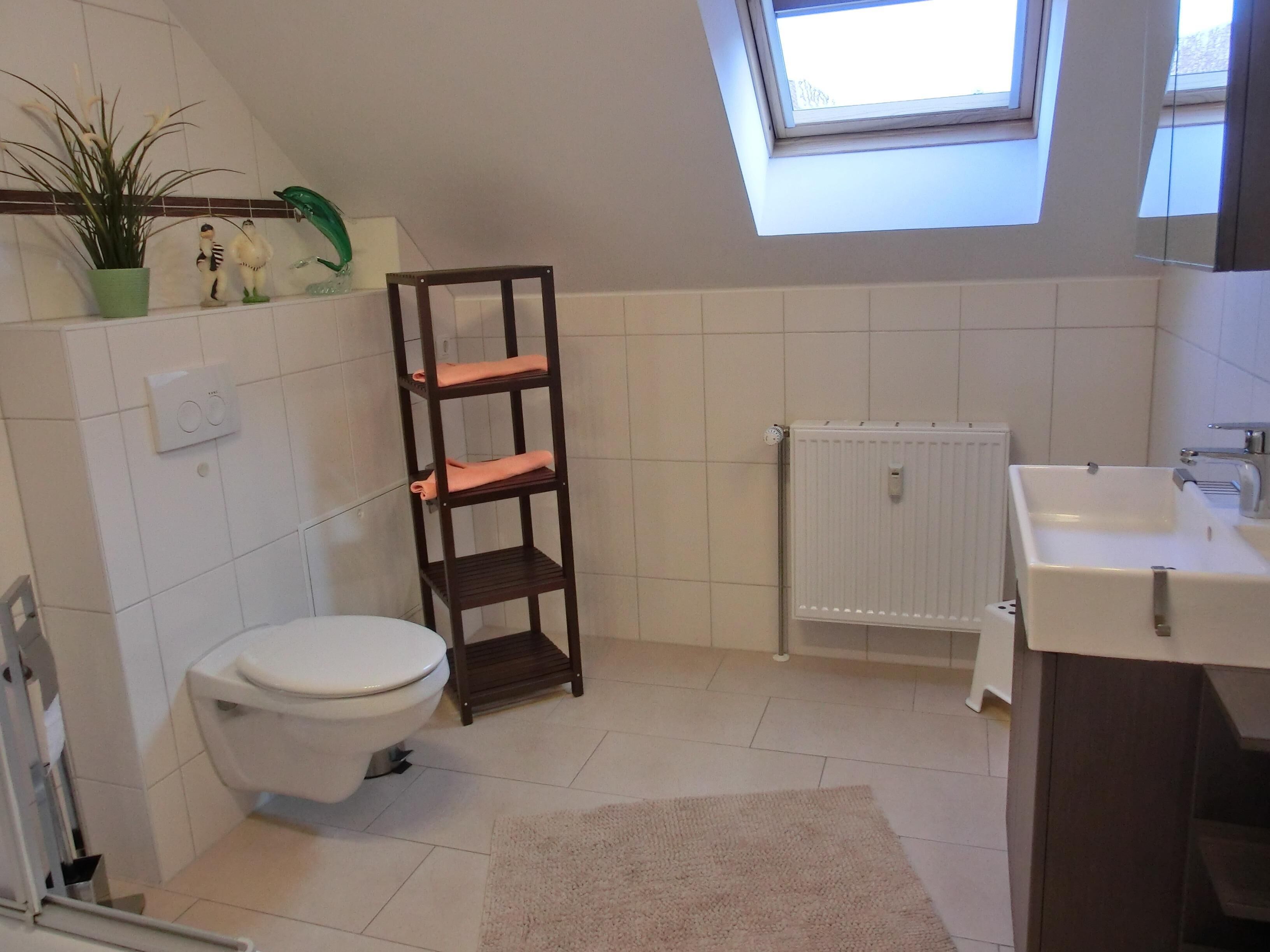 Ein Badezimmer mit Toilette, Heizkörper, Waschbecken, Ablagefläche mit Handtüchern und einem Oberlicht.