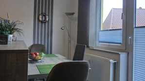 A dining area with a table, chairs, a bowl of fruit, a potted plant, and a wall clock. - 2- Zi.-fewo für 2 Personen mit Balkon und Wlan (Graal-Müritz)