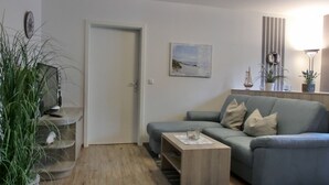 A living room with a grey sofa, a coffee table, a TV on a stand, a door, and a painting on the wall. - 2- Zi.-fewo für 2 Personen mit Balkon und Wlan (Graal-Müritz)