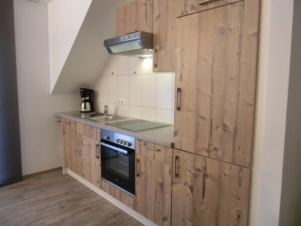 A compact kitchen with wooden cabinets, a built-in oven, a stainless steel sink, and a coffee maker.
