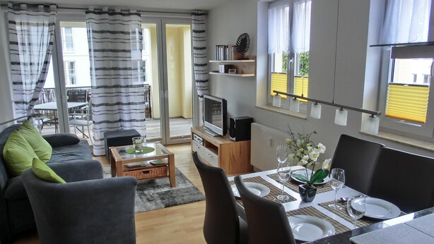 Ein modernes Wohnzimmer mit einer Couch, einem Esstisch für zwei Personen, einem Fernseher und einem Bücherregal.