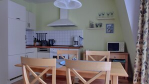 A compact kitchen with white cabinets, a wooden dining table, and chairs. There is a microwave, a kettle, and a coffee maker on the counter. - 3-zimmer-appartement im 1. OG mit Wlan (Graal-Müritz)