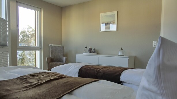 Ein Hotelzimmer mit zwei Betten, einem Sessel, einer weißen Kommode und einem Bild an der Wand.