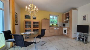 Een moderne keuken met houten kastjes, een eettafel met stoelen, een kroonluchter en een televisie.