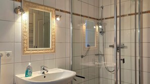 Een badkamer met een wit wastafelblad, een spiegel met een sierlijk omlijsting, en een douchecabine met glazen wanden.