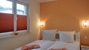 Une chambre d’hôtel avec deux lits, une fenêtre avec des stores et des lampes fixées au mur.
