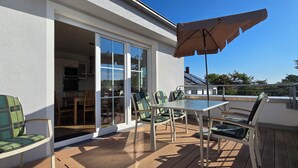 Una terrazza con tavolo e sedie, una porta scorrevole in vetro che dà su una cucina, e un grande ombrellone per l'ombra.