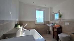 Un bagno moderno con vasca, lavandino, WC e una finestra che lascia entrare luce naturale.