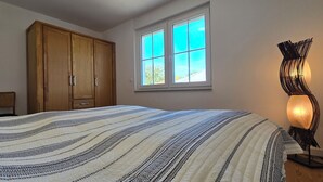 Una camera da letto con un letto grande, un armadio in legno, una finestra con vista e una lampada da terra.