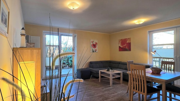 Ett vardagsrum med en soffa, ett matbord med stolar, en lampa och ett fönster med utsikt över omgivningen.