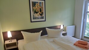 Une chambre d’hôtel avec un lit, deux oreillers, une table de chevet avec une lampe, un tableau encadré au mur et une fenêtre donnant sur un paysage.