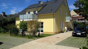 Une maison jaune à deux étages, avec un toit en tuiles, un balcon et une allée pavée.