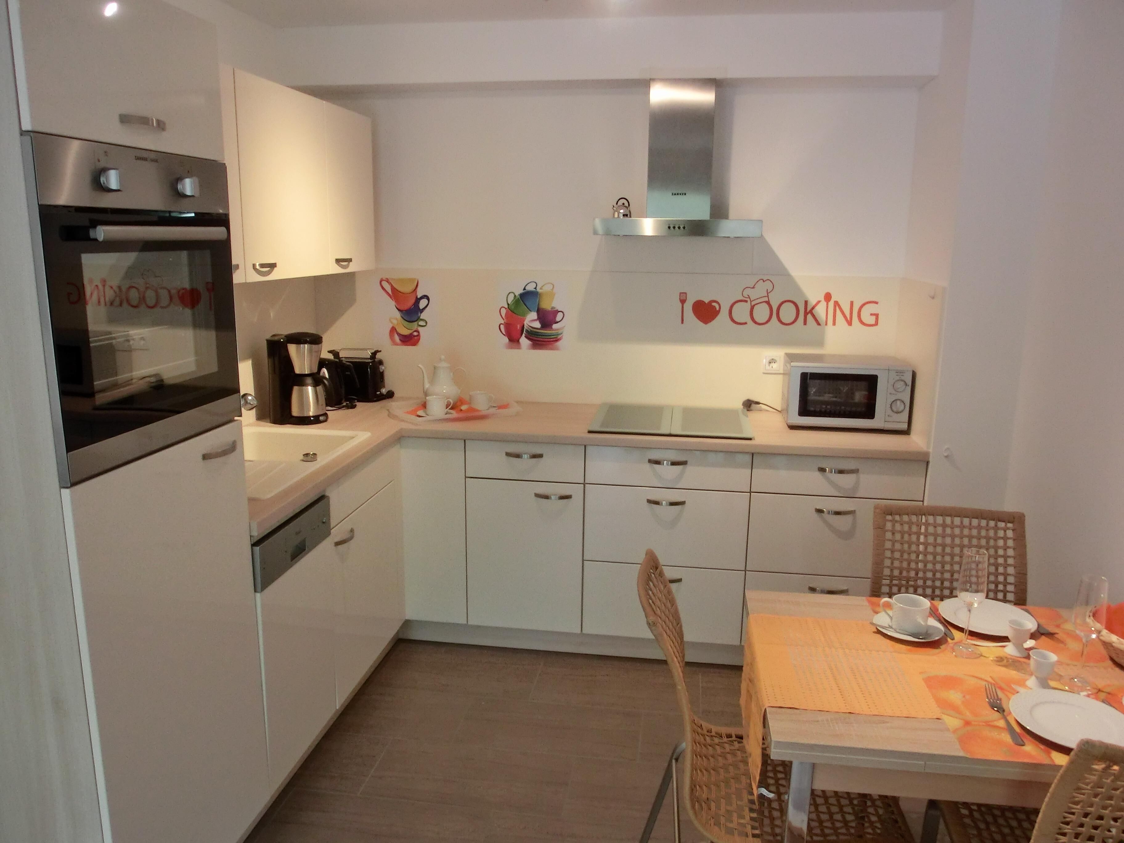 Cocina compacta con horno, microondas y cafetera. Hay una mesa de comedor con platos, tazas y cubiertos.