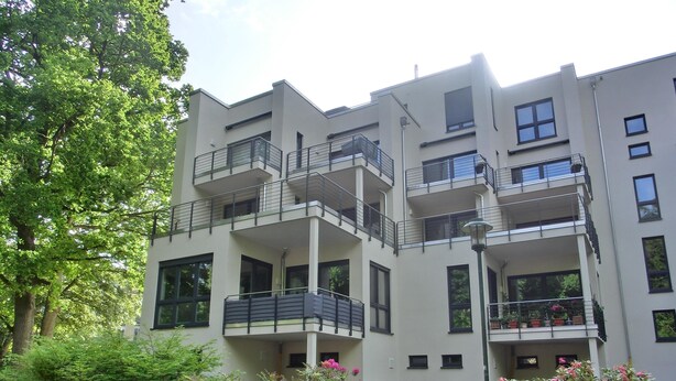 Un edificio residencial de varios pisos con balcones, ventanas amplias y vegetación circundante.