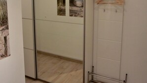 Una habitación con armario corredera con espejo, un perchero de madera y una ventana pequeña con vista a la playa.
