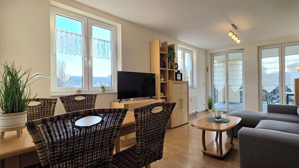 Een moderne woonkamer met een bank, een televisie, rieten stoelen, een salontafel en een boekenkast.