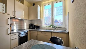 Een compacte keuken met een kookplaat, oven, magnetron en een raam met gordijnen.