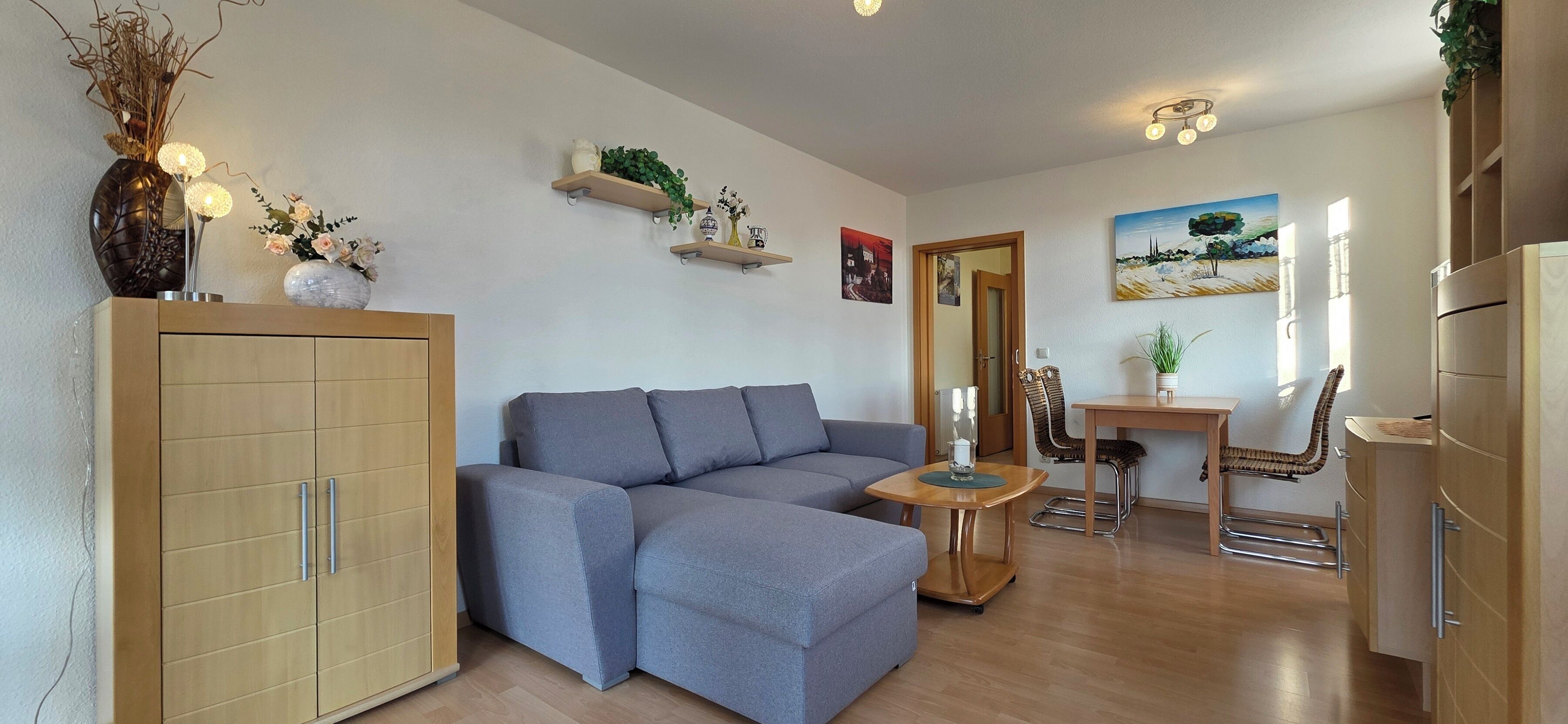 Un salon moderne avec un canapé gris, des meubles en bois et un coin repas comprenant une petite table et des chaises.