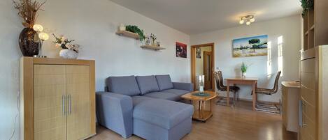 Un salon moderne avec un canapé gris, des meubles en bois et un coin repas comprenant une petite table et des chaises.