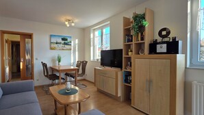 Een woonkamer met een bank, een eettafel met stoelen, een televisie en een boekenkast.