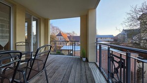 Een houten terras met metalen stoelen en een hek, met uitzicht op een woonwijk met huizen en bomen.
