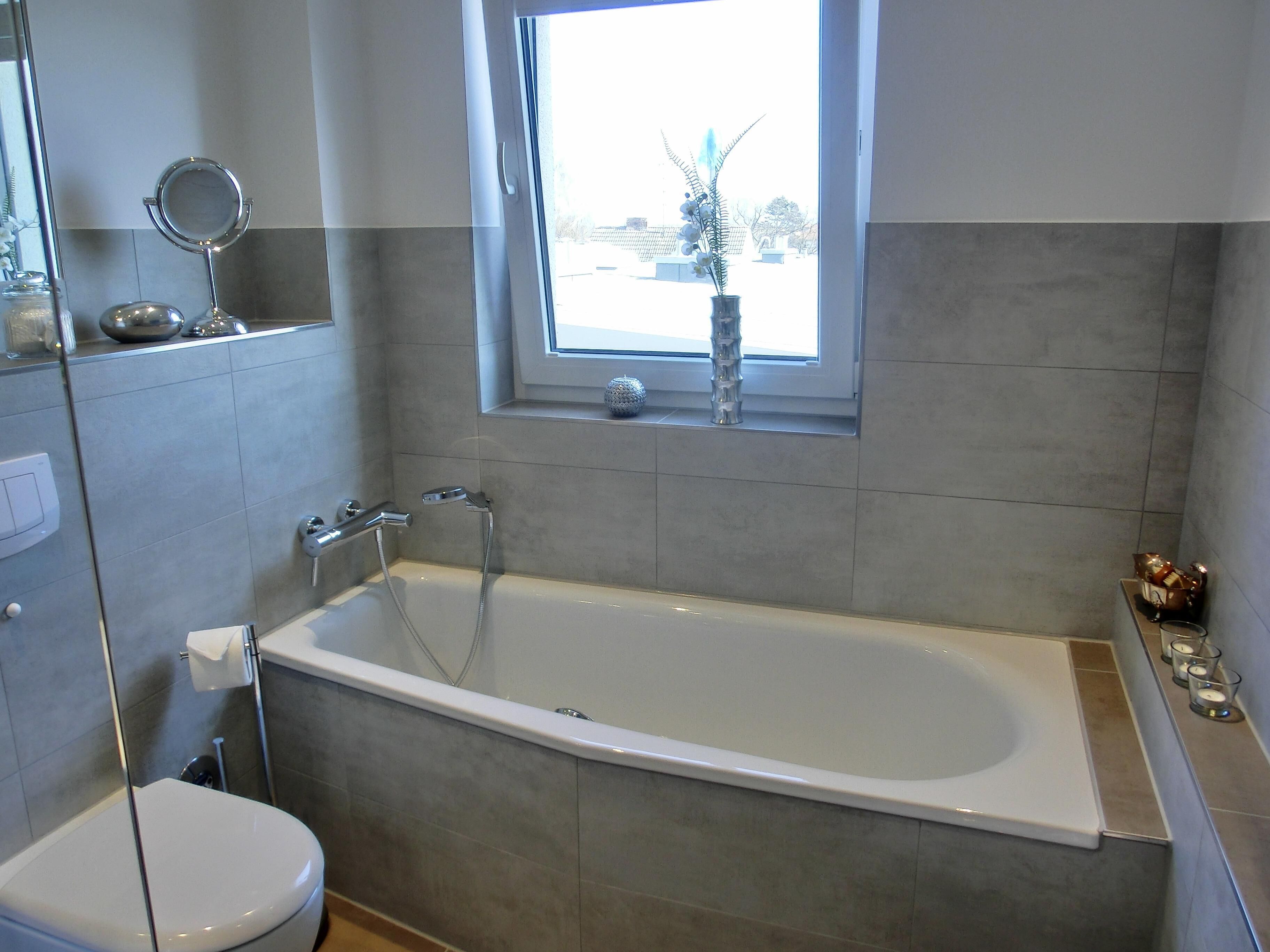 A modern bathroom with a bathtub, toilet, and a window.