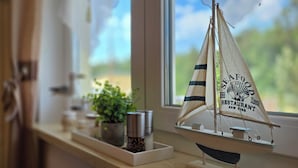 Um modelo de barco à vela em um parapeito de janela, com vista para o verde lá fora.