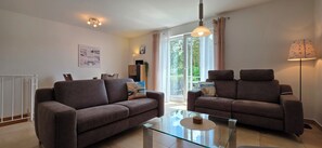 A living room with two sofas, a glass coffee table, a ceiling light, and a view through a large window. - 3-zimmer-fewo mit 2 SZ für 4 Pers. und Wlan (Graal-Müritz)