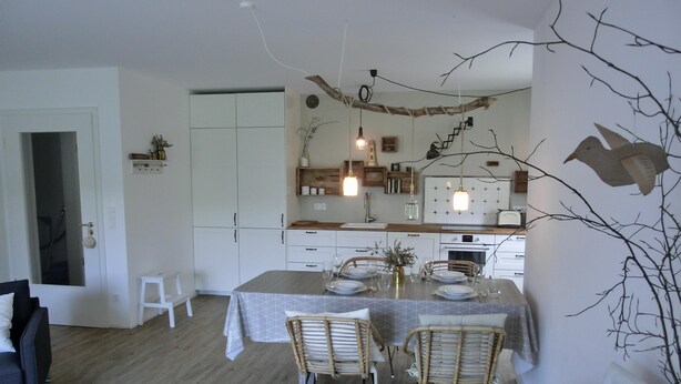 A dining area with a table set for four, surrounded by wicker chairs, in a room with a wooden floor and white walls. - Strandnahe 3-zimmer-ferienwohnung für 4 Pers. mit Terrasse (Graal-Müritz)