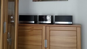 A wooden cabinet with a flat-screen TV and speakers on top, a glass-fronted cabinet door, and a painting of a beach scene on the wall. - Strandnahe 2-zi.-fewo mit Balkon für 3 Personen in Ruhiger Lage (Graal-Müritz)