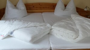 A bed with white bedding and pillows, a wooden headboard, and a painting of a beach scene on the wall above. - Strandnahe 2-zi.-fewo mit Balkon für 3 Personen in Ruhiger Lage (Graal-Müritz)