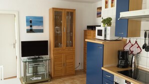 A compact kitchen with a microwave, coffee maker, and a TV on a glass shelf. - Strandnahe 2-zi.-fewo mit Balkon für 3 Personen in Ruhiger Lage (Graal-Müritz)